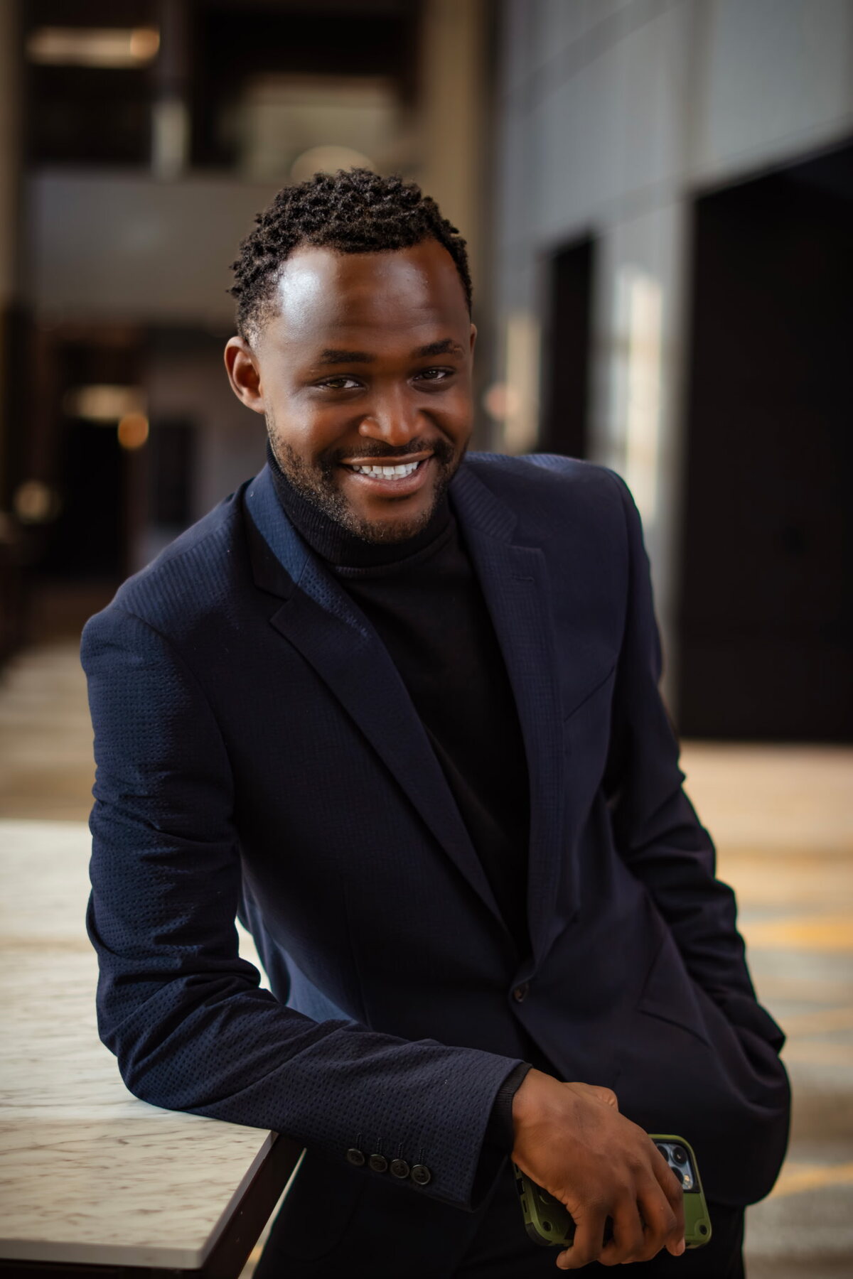 Habi Gasigwa smiling, in a navy blazer and black turtleneck